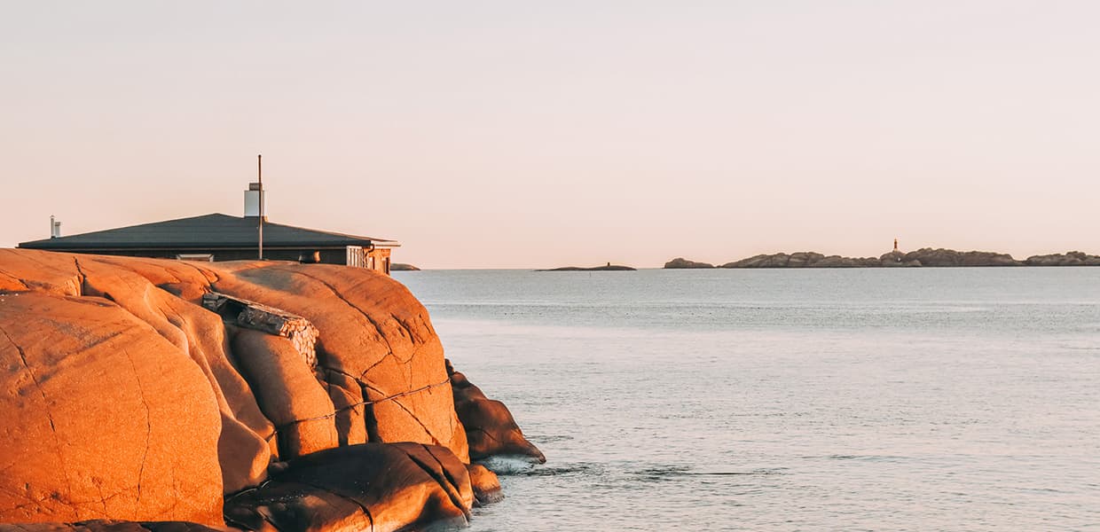 svaberg og hav med et fyr i horisonten